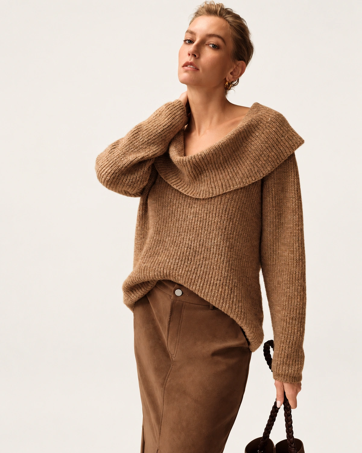 Vista lateral três quartos da modelo com suéter tricot camel exibindo caimento fluido e gola ampla.