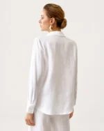 Vista posterior da modelo em perfil vestindo camisa de puro linho off-white destacando caimento solto