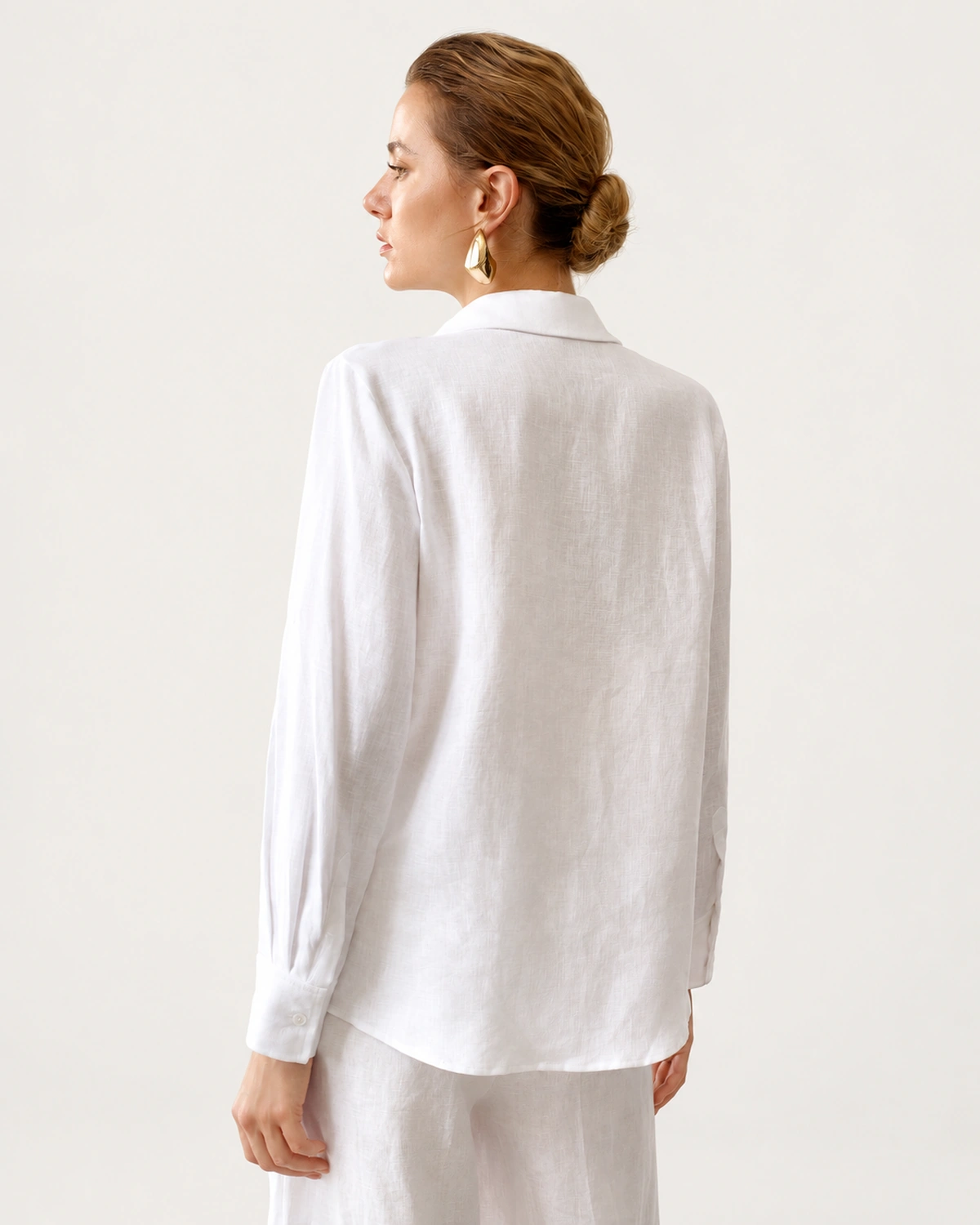 Vista posterior da modelo em perfil vestindo camisa de puro linho off-white destacando caimento solto
