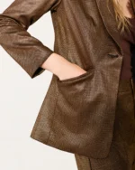 Plano detalhe do blazer alfaiataria bronze metalizado destacando acabamento de bolso e manga.
