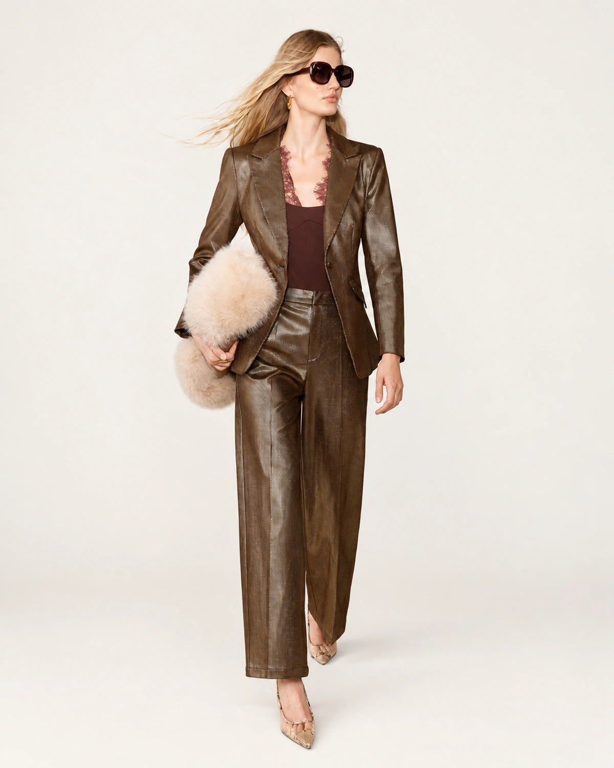 Modelo caminhando com blazer de alfaiataria bronze metalizado estruturado com calça pantalona em estúdio.