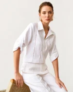 Modelo sentada em banco de palha vestindo camisa de puro linho off-white