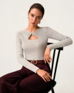 Modelo sentada em cadeira de estúdio vestindo suéter de tricot canelado cinza-mescla e calça de alfaiataria