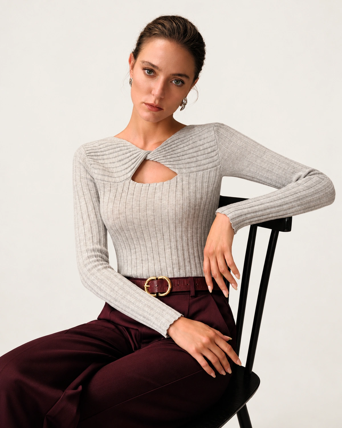 Modelo sentada em cadeira de estúdio vestindo suéter de tricot canelado cinza-mescla e calça de alfaiataria
