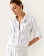 Modelo vestindo camisa alfaiataria em puro linho off-white com entremeios vazados e calça de alfaiataria