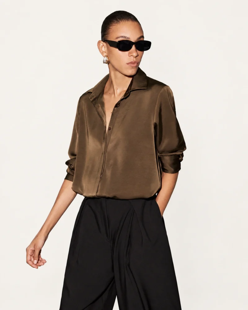 Camisa feminina acetinada em tom café com vista frontal oculta e gola estruturada usada com calça alfaiataria preta no estúdio mineral Peaker.