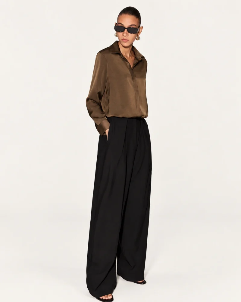 Modelo de corpo inteiro em estúdio mineral vestindo camisa clássica acetinada café e calça pantalona de alfaiataria preta.