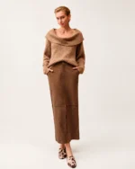 Modelo vestindo suéter tricot canelado camel com gola dobrada ampla e saia de suede marrom em estúdio.