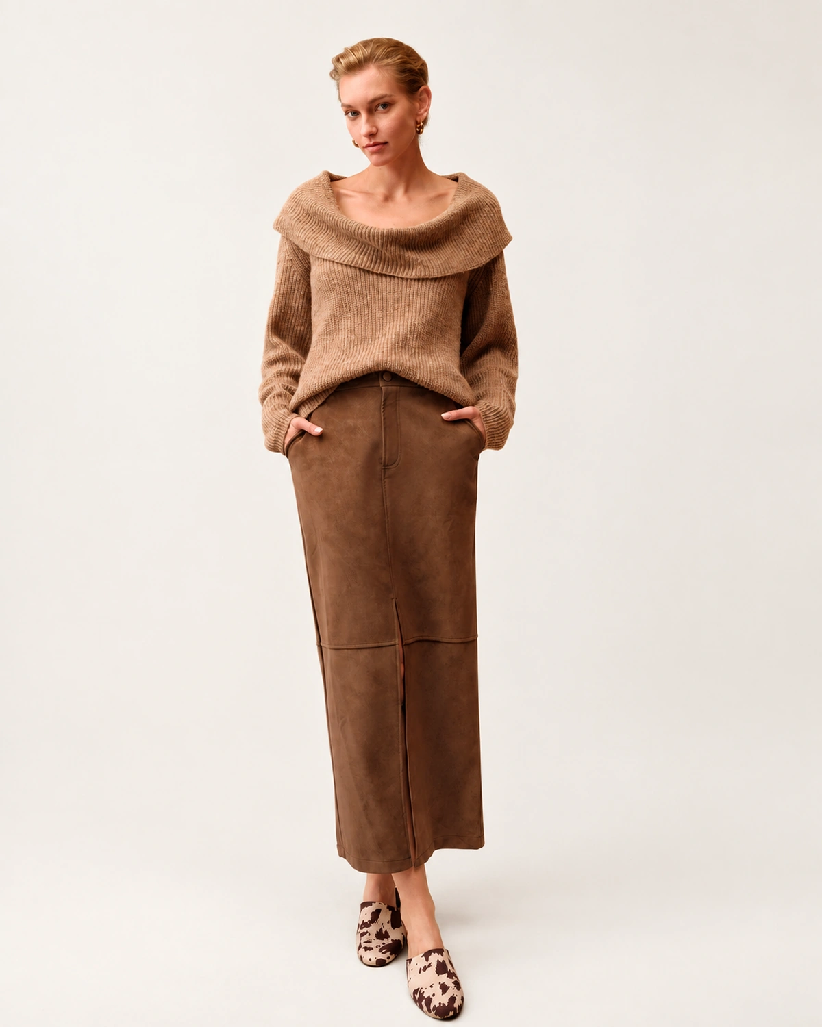 Modelo vestindo suéter tricot canelado camel com gola dobrada ampla e saia de suede marrom em estúdio.