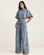 Modelo em pé vestindo conjunto jeans pantalona e cropped evasê em jeans claro com mão no bolso