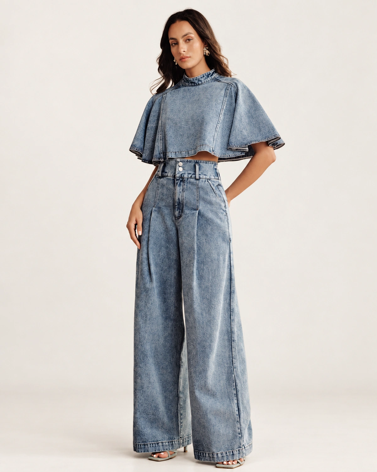 Modelo em pé vestindo conjunto jeans pantalona e cropped evasê em jeans claro com mão no bolso