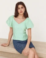 Foto editorial em plano médio da modelo sentada em mureta de travertino com blusa texturizada Verde-Menta.
