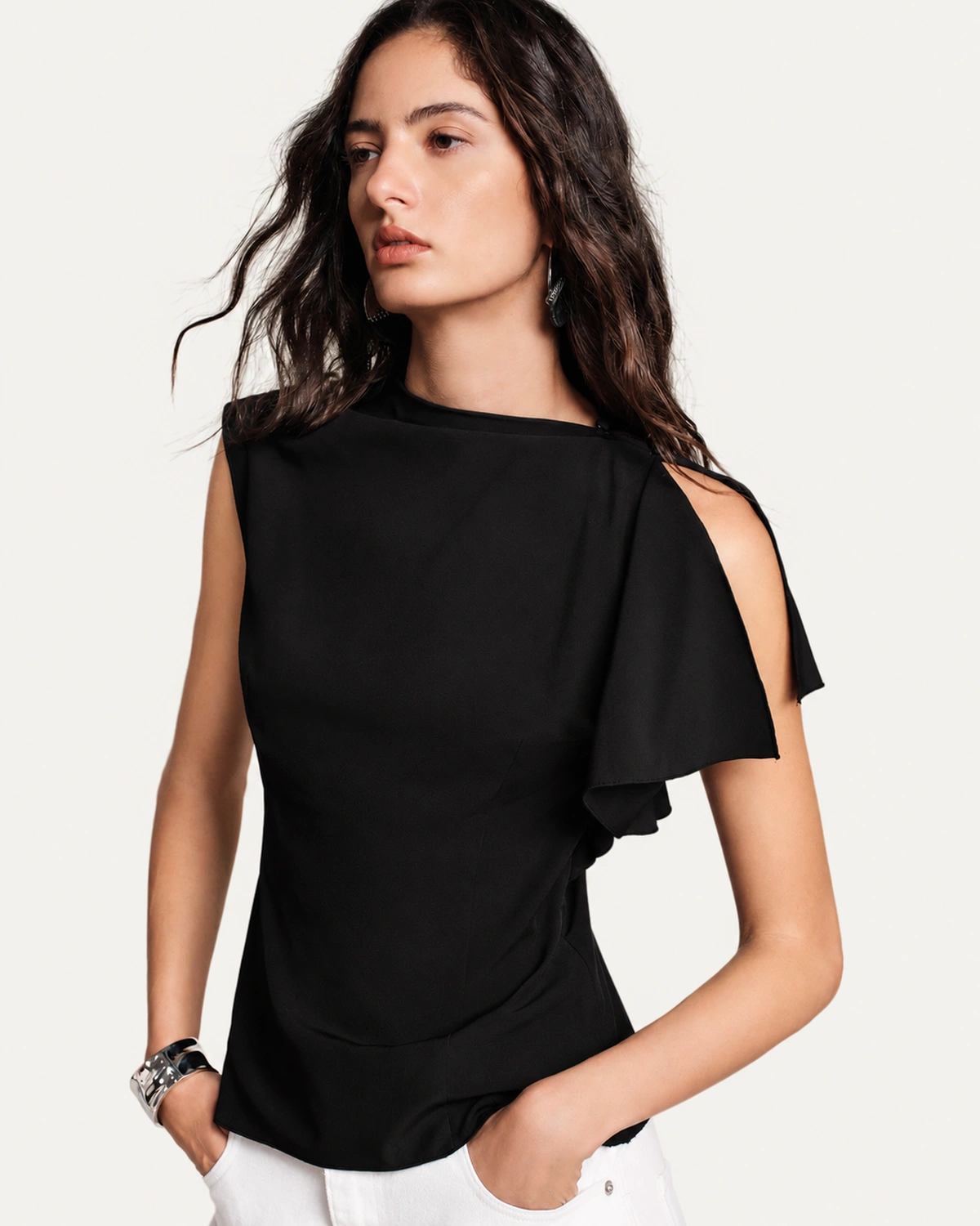 Modelo vestindo blusa assimétrica em crepe fluido preta com calça branca em estúdio mineral