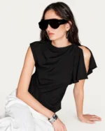 Editorial sentado da modelo vestindo blusa assimétrica preta apoiada no piso mineral