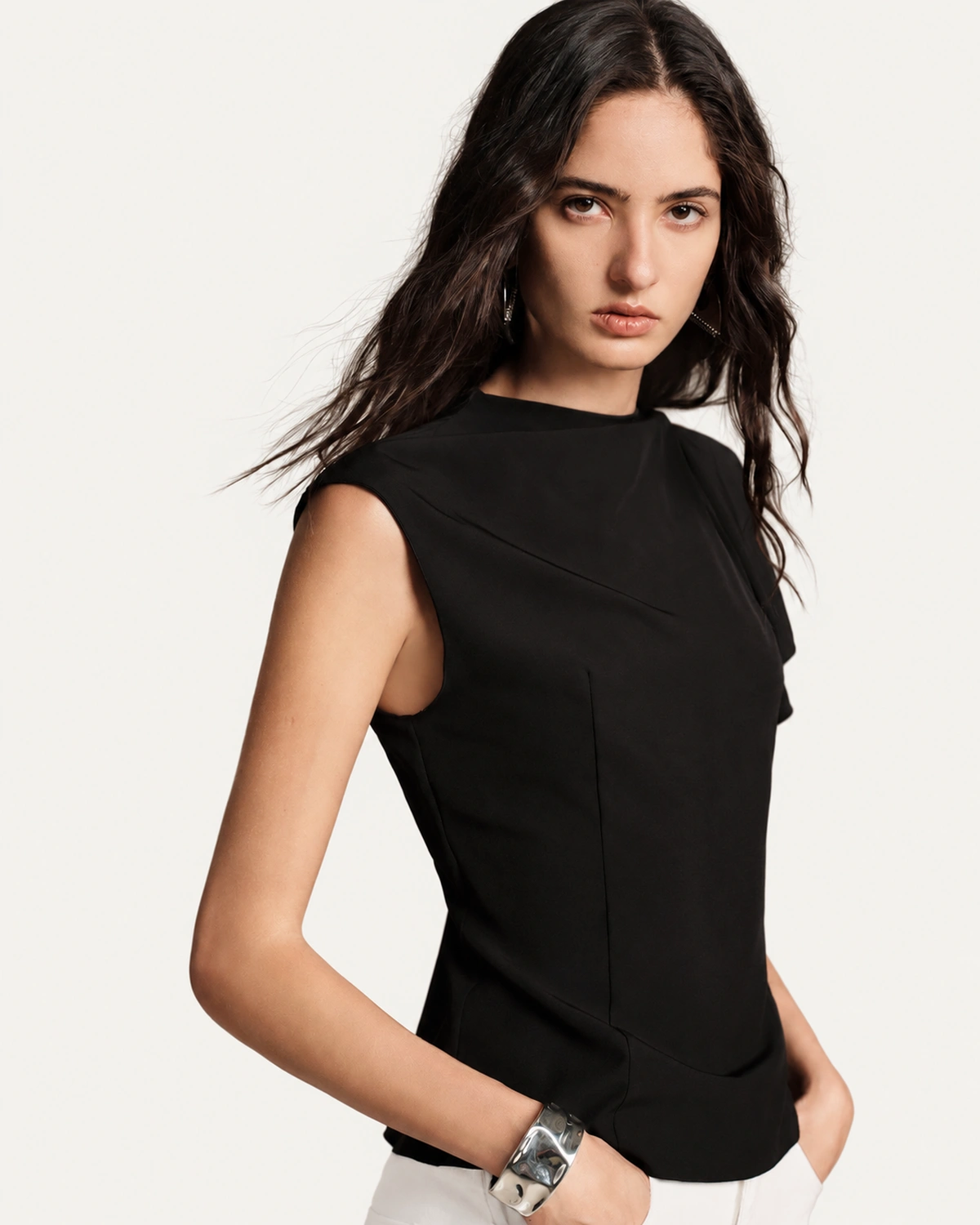 Vista frontal da blusa preta assimétrica com pences e costuras de alfaiataria em estúdio mineral