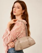 Modelo em estúdio mineral vestindo conjunto paisley e segurando a bolsa meia-lua croco areia sob o braço.