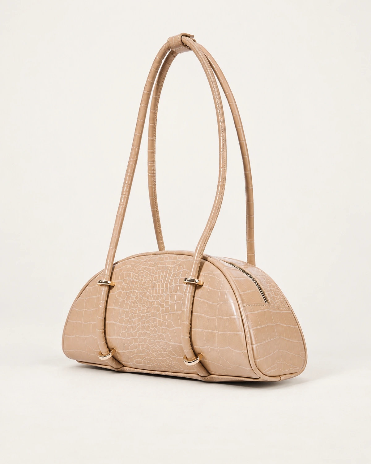 Bolsa meia-lua em PU textura croco areia apoiada no solo mineral em vista três quartos.