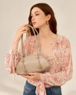 Modelo segurando a bolsa meia-lua croco areia à frente do corpo em estúdio mineral.