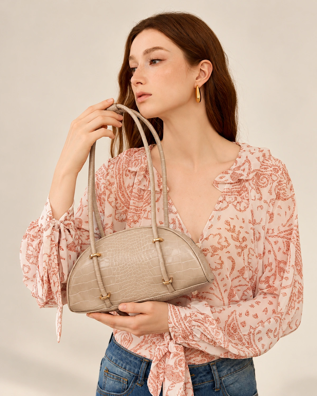 Modelo segurando a bolsa meia-lua croco areia à frente do corpo em estúdio mineral.