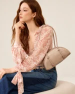 Retrato da modelo com a bolsa meia-lua croco areia apoiada ao lado.