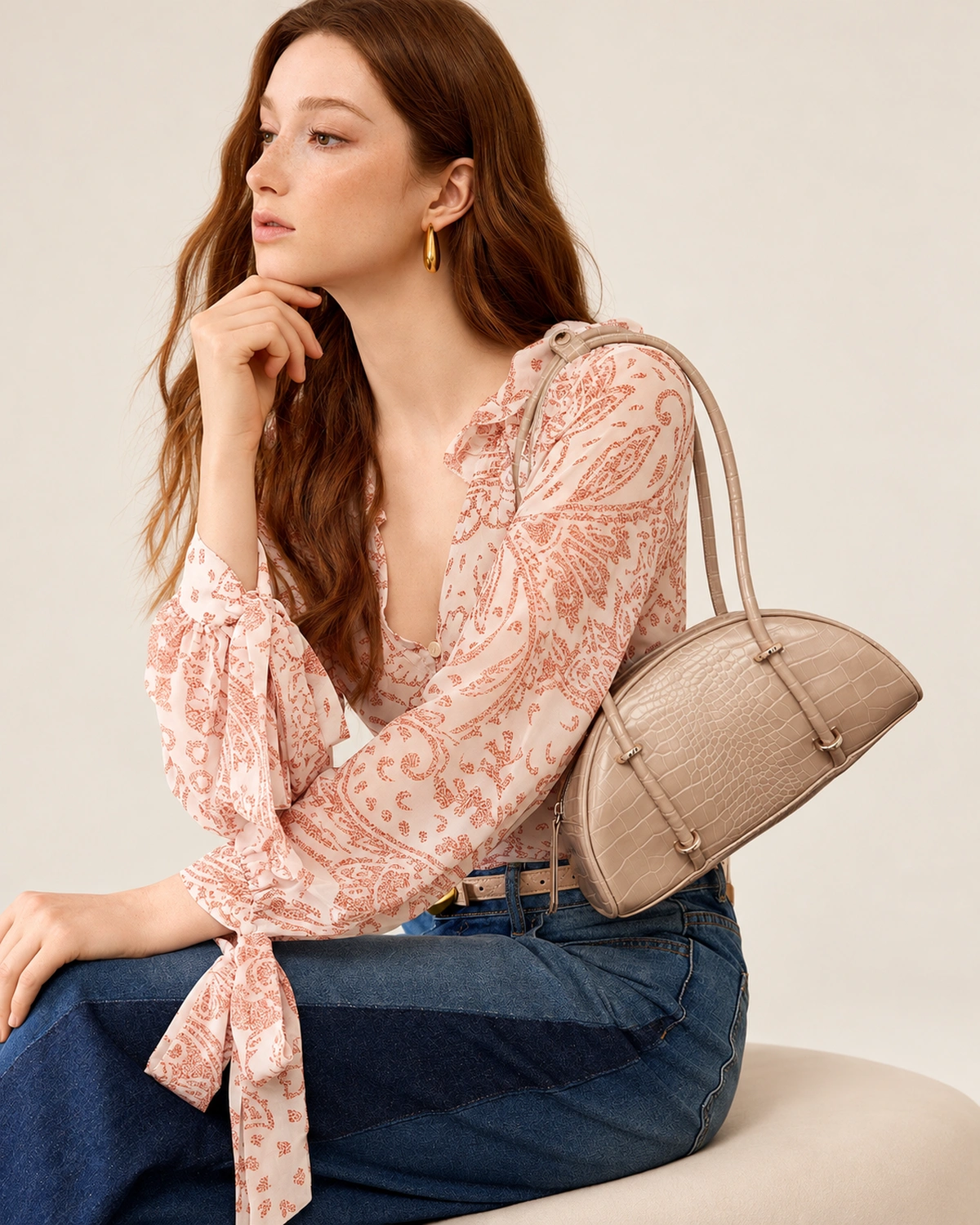 Retrato da modelo com a bolsa meia-lua croco areia apoiada ao lado.