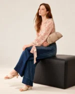 Modelo sentada em banco editorial com a bolsa meia-lua croco areia ao lado.