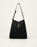 Bolsa shoulder bag preta estruturada com fecho de argolas e fivela metálica dourada no solo mineral