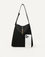 Bolsa shoulder bag preta com smartphone em escala no piso mineral comprovando capacidade para itens pessoais