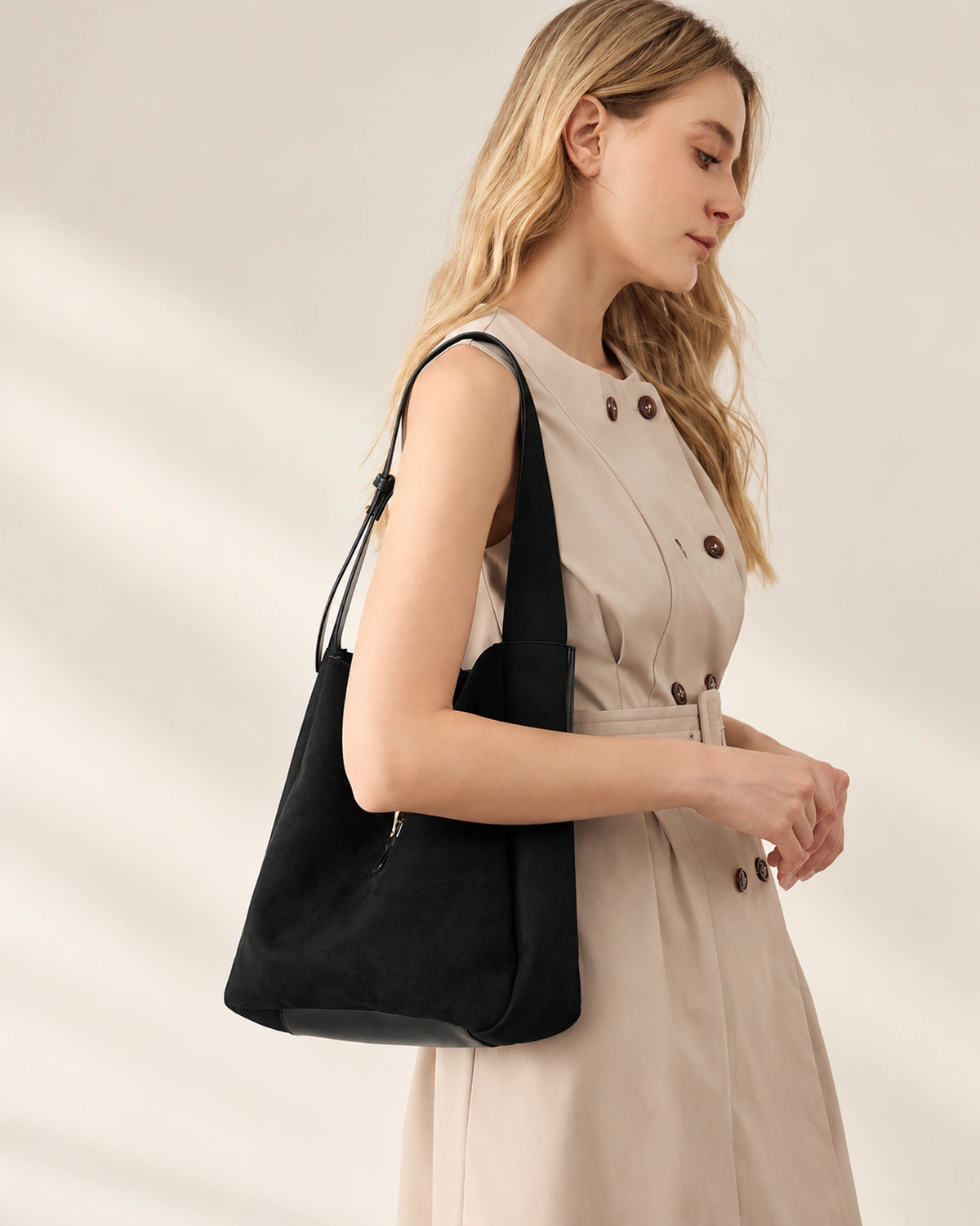 Modelo em vestido bege de perfil segurando a bolsa shoulder bag estruturada preta junto ao quadril