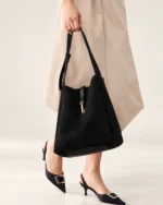 Detalhe da modelo segurando a alça longa regulável da bolsa shoulder bag preta ao caminhar