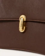 Detalhe do fecho dourado escultural e textura do couro liso da bolsa Café.