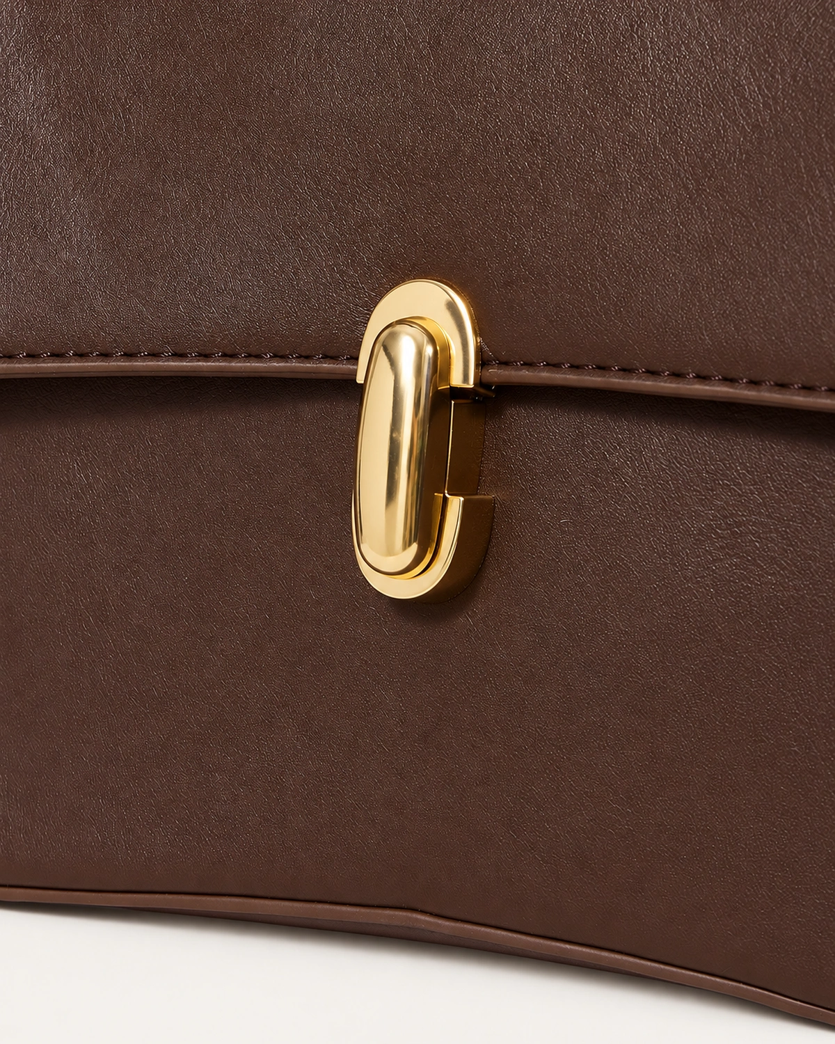 Detalhe do fecho dourado escultural e textura do couro liso da bolsa Café.
