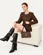 Modelo sentada em poltrona com bolsa tiracolo Café em couro liso.