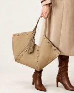 Modelo em look sofisticado segurando a bolsa tote em suede marrom na mão em composição de alfaiataria