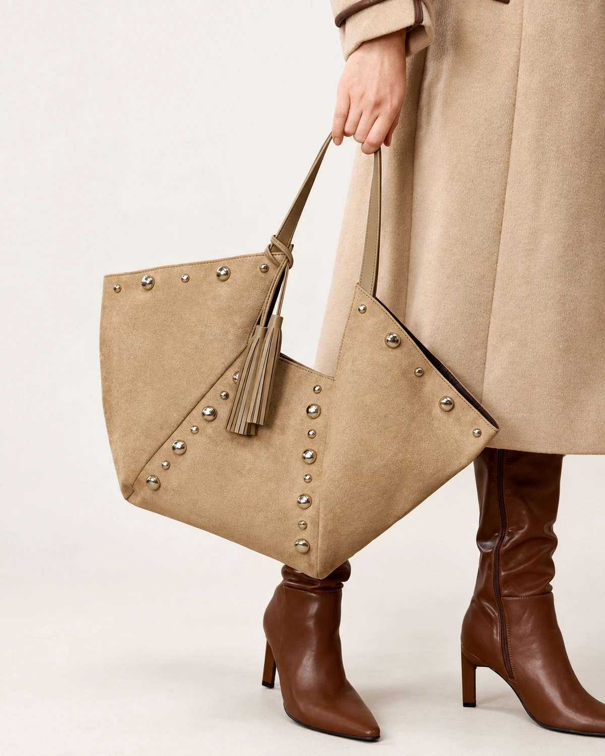 Modelo em look sofisticado segurando a bolsa tote em suede marrom na mão em composição de alfaiataria