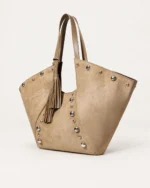 Bolsa tote em suede aveludado marrom conhaque com rebites metálicos prateados apoiada no solo mineral