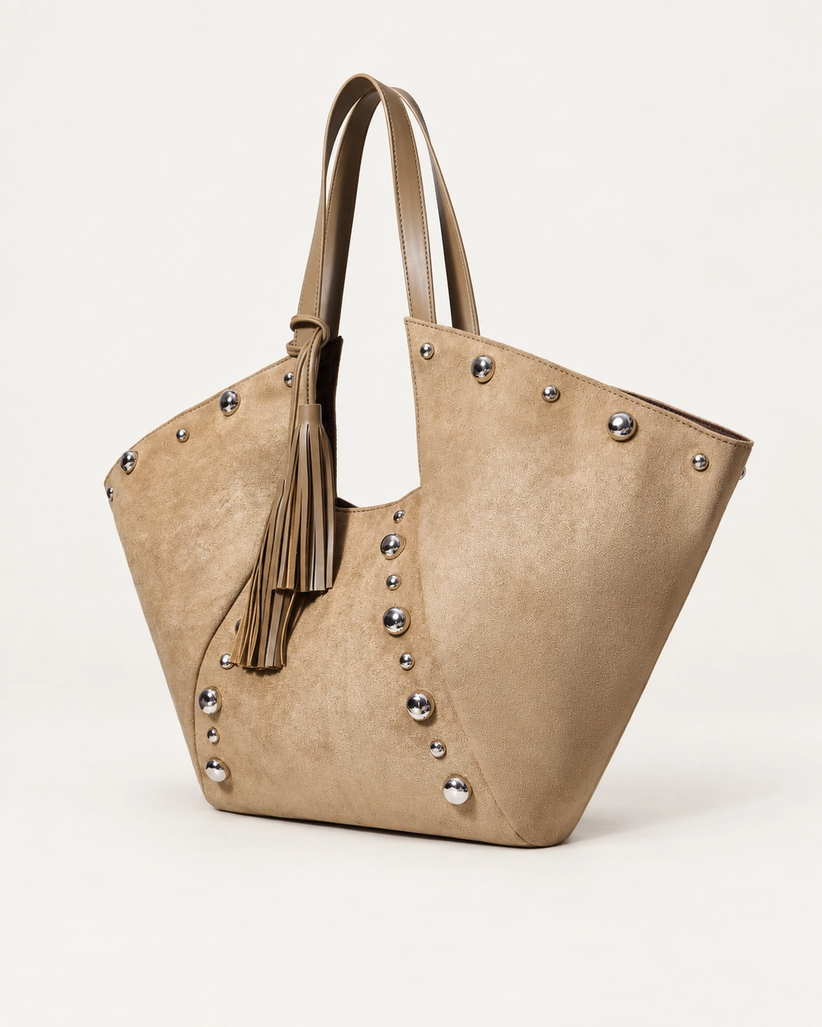 Bolsa tote em suede aveludado marrom conhaque com rebites metálicos prateados apoiada no solo mineral
