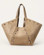 Bolsa tote em suede marrom conhaque em perspectiva destacando abas laterais expandidas no solo mineral