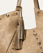 Close aproximado da bolsa tote destacando a textura do suede aveludado, rebites esféricos prateados e barbicacho de cour