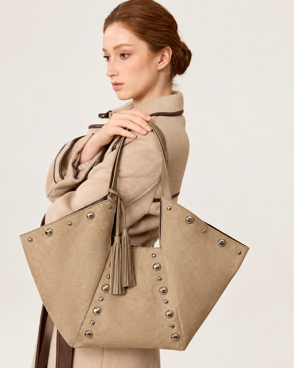 Modelo ruiva elegante usando a bolsa tote em suede com rebites metálicos no ombro em sobretudo de lã bege