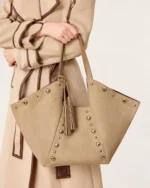 Plano médio da modelo segurando a bolsa tote em suede com sobretudo de lã em estúdio mineral