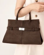 Plano médio da modelo segurando a bolsa tote marrom café no antebraço em look elegante creme de alfaiataria