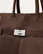 Close aproximado da bolsa tote marrom café destacando o fecho torniquete prateado e a textura da camurça