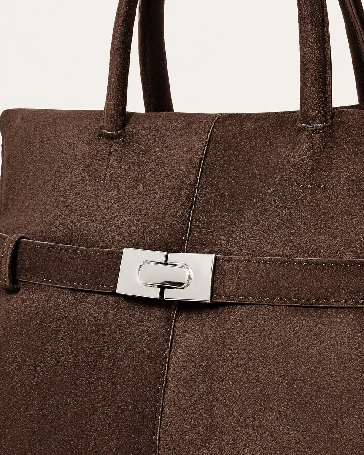 Close aproximado da bolsa tote marrom café destacando o fecho torniquete prateado e a textura da camurça