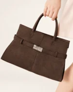 Plano detalhe da mão da modelo segurando a alça da bolsa tote marrom café ao lado do corpo