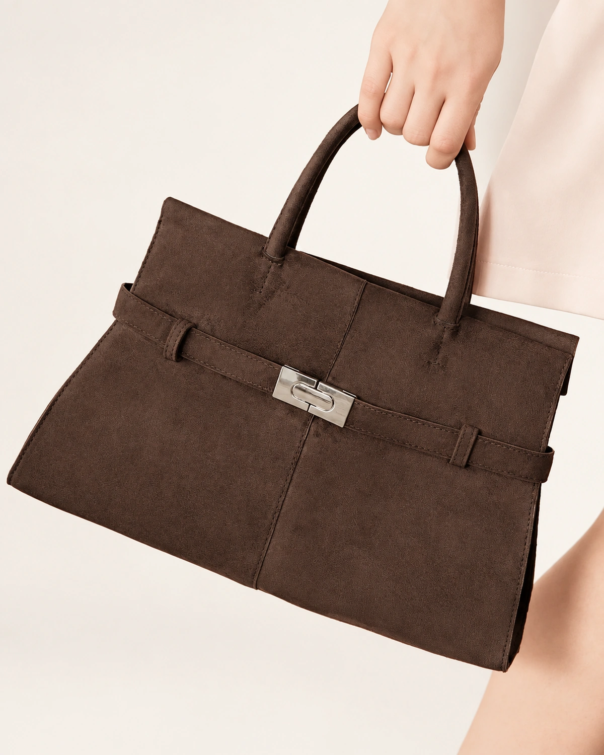 Plano detalhe da mão da modelo segurando a alça da bolsa tote marrom café ao lado do corpo