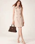 Modelo ruiva de corpo inteiro em vestido trench coat bege segurando a bolsa tote marrom café