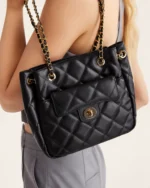Plano detalhe da bolsa tote preta matelassê em couro acolchoado no ombro da modelo em estúdio mineral