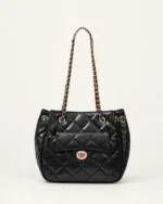 Bolsa tote acolchoada preta em matelassê com bolso frontal e alças de corrente dourada no solo mineral