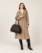 Modelo de corpo inteiro com casaco bege e botas pretas carregando a bolsa tote em suede marrom no estúdio mineral